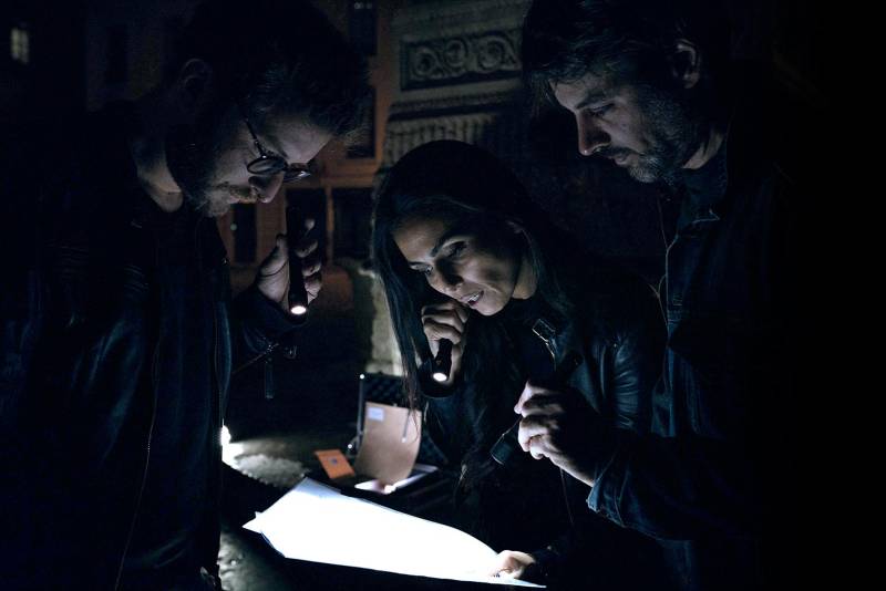 Trois participants éclairent une carte avec des lampes torches lors d'une traque nocturne avec Mimesis Aventure